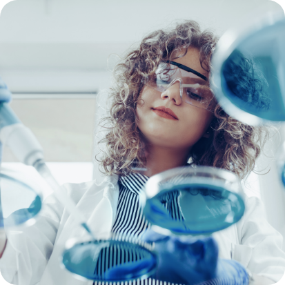 A woman wearing safety goggle and filling petri dishes.