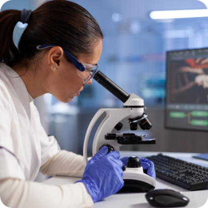A woman wearing purple gloves and looking into a microscope