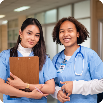 Two women in scrubs. One is holding a clipboard and the other has a stethoscope around her neck.